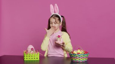 Genç liseli kız kameranın önünde hava öpücüğü verirken doldurulmuş tavşan oyuncağı için şenlikli güzel düzenlemeler yapıyor. Neşeli genç çocuk Paskalya kutlaması için heyecanlanıyor. Kamera A.