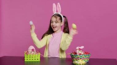Hevesli genç bir kız, pembe arka planda boyalı paskalya yumurtalarını kullanarak kameranın önünde dikizcilik yapıyor. Neşeli, sevimli çocuk bahar bayramı şenliği için heyecanlanıyor. Kamera A.