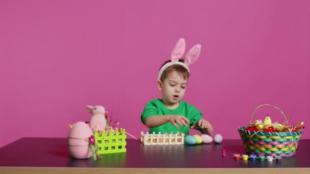 Szczęśliwy Maluch Króliczymi Uszami Aranżujący Kosz Wypełniony Malowanymi Jajkami Tworzący — Wideo stockowe