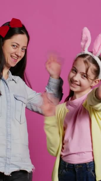 微笑着快乐的母亲和小女孩在镜头前挥手 开心地享受着东方节日的庆祝活动 一个快乐的女学生和她妈妈在工作室里摆姿势打招呼摄像头B — 图库视频影像