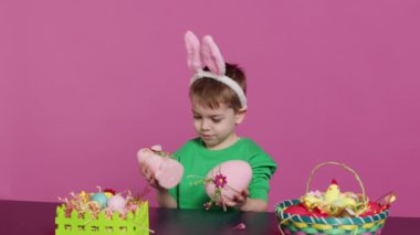 Paskalya bayramı kutlaması için yaratılan el yapımı süslemeleri sunan küçük memnun çocuk. Tavşan kulaklı genç bir çocuk boyalı süslemeler, bir tavşan ve bir yumurta gösteriyor. Kamera A.