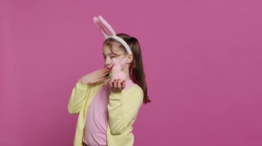 Güzel bir tavşan oyuncağı tutan ve stüdyoda öpücükler saçan neşeli liseli kız Paskalya bayramı etkinliği için şenlikli süslemelerle sevimli oluyor. Tavşan kulaklı ve örgülü mutlu çocuk. Kamera A.