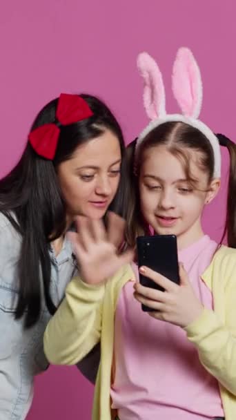 垂直ビデオリトル女子高生と彼女の母親は スタジオでのビデオコールミーティングで話し ウェブカムで振り 家族とチャットしました テレコンファレンスチャットのためのスマートフォンを使用してかわいいプルーとマザー — ストック動画
