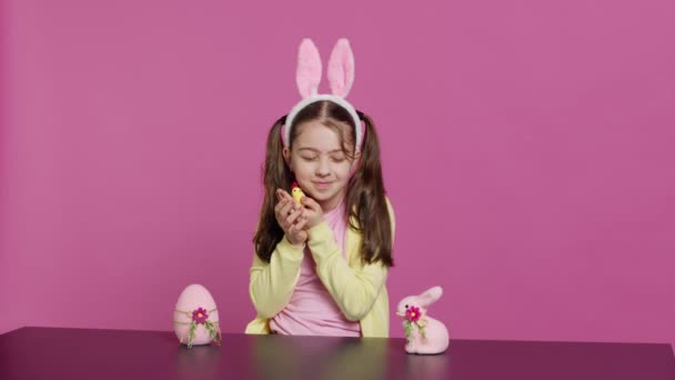 スタジオでお祝いのイースターの装飾で遊ぶ楽しい少女は ひよこ ウサギ 卵とのアレンジを作成します カラフルな装飾を示すバニーの耳を持つかわいいトッドラー カメラ — ストック動画