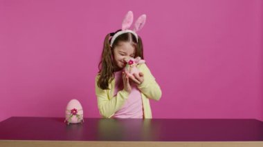 Güzel paskalya süslemeleriyle oynayan küçük tatlı bir kız bahar bayramını kutlamak için şenlikli süsler yapıyor. Sevimli pembe tavşan ve yumurta sunan neşeli çocuk. Kamera B.