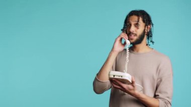 Ortadoğulu mutlu adam telefon görüşmesinde en iyi arkadaşıyla sohbet ediyor. Sabit telefon kullanarak arkadaşla iletişim kuran neşeli kişi, stüdyo arkaplanı üzerinden izole edilmiş, kamera A
