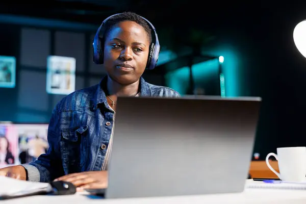 ラップトップとノートを書くことでワイヤレスヘッドフォンを着用した黒人女性 アフリカ系アメリカ人女性学生 ヘッドセット付き オンライン ウェビナー パソコンでオーディオコースを聞く — ストック写真