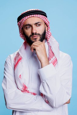 Geleneksel giyinmiş Müslüman bir adam dalgın dalgın bakıyor. Sorgulanan Arap adam tobe ve ghutra başörtüsü takıyor. Düşünme pozu veriyor.