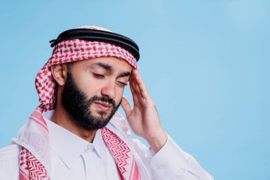 Geleneksel giysiler içinde Müslüman bir adam migren krizi geçirirken rahatsızlığını ifade ediyor ve tapınağı ovuyor. Arap adam ghutra başlık takıyor, başı ağrıyor ve acı çekiyor.