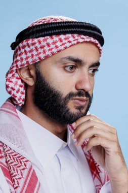 Geleneksel başlıklı Müslüman adam düşünüyor ve çözüm düşünüyor. Arap bir insan, başörtüsü takıyor, çenesini ovalıyor ve yoğun bir ifadeyle yüzünü çeviriyor.