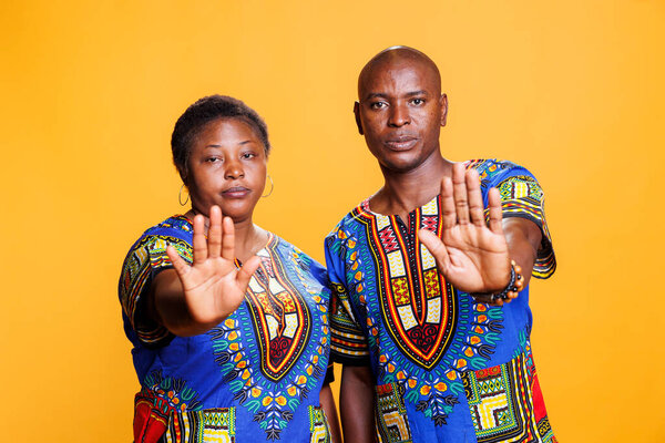 Confident man and woman showing stop gesture with palms studio portrait. African american couple showcasing refuse signal and looking at camera with serious face expression
