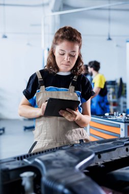 Araba servisindeki teknisyen, elektrik sistemini tamir ettikten sonra müşterinin faturasını hesaplamak için tablet kullanır. Becerikli garaj çalışanı müşteri aracına hizmet ettikten sonra son maliyetleri hesaplıyor