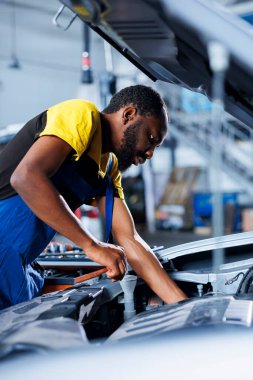 Mühendis, otomotiv performansını ve güvenliğini sağlamak için gelişmiş mekanik araçlar kullanarak araba aküsünü inceliyor. BIPOC garaj çalışanı yıllık araç kontrolü yapıyor