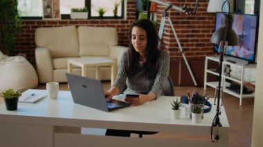 Mutlu kadın online alışveriş yapıyor, dizüstü bilgisayarına kredi kartı bilgilerini dikkatlice yazıyor. Hintli kişi web sitesine ödeme metodu eklerken rahat, sıcak bir evde, kamera bir ekran görüntüsü