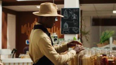 Afrikalı Amerikalı satıcı, yerel çiftçilerin pazar ürünlerini hazırlıyor, yeniden kullanılabilir kavanozlardaki ürünleri sergiliyor. Mahallenin süpermarketinde mal satan bir genç. Kamera A.