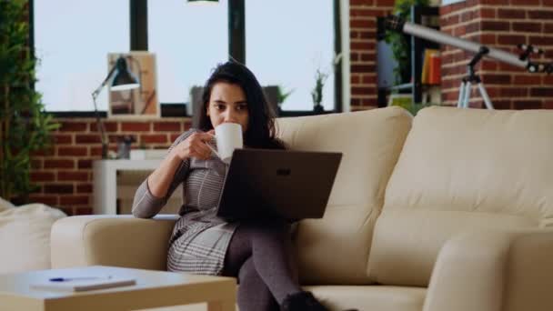 ソファーに横たわるテレワーカーは リモートで個人のオフィスでタスクを実行しながらコーヒーを飲んでいます ストレスを感じるフリーランサー ラップトップ カメラBにデータを入力しながらリラックスするホットドリンクを楽しむ — ストック動画