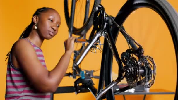 愉快的技师用旋转踏板检查自行车的性能 微笑专家确保自行车轮子上的轮胎在橙色工作室背景下在检查时的正常功能 相机B — 图库视频影像