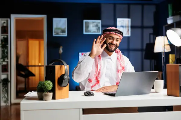 イスラム教徒の男性がパソコンで振りながら デスクに座ってビデオ通話をする デジタルノートパソコンを使ってデジタルテクノロジーに没頭しながら探求し チャットし 研究しています — ストック写真