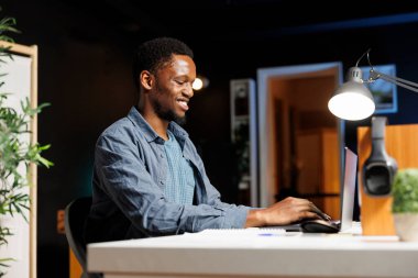 İş maliyeti ve gelir unsurlarını hesaplayan finans uzmanı, gelir ve giderler arasında bir denge oluşturmak için evden çalışıyor. Raporlarla muhasebe yapan Afrikalı Amerikalı bir adam..