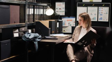 Kararlı özel dedektif ayrıntılı bir soruşturma yapmak için raflardan dosyaları alır. Laptop ve araştırma kağıtlarıyla beyaz kadın ajan, kanıtları analiz eder ve bilgi toplar. Üçayak atışı.