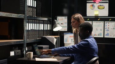 Two private investigators studying forensic evidence on laptop and discussing criminal information in office. Black policeman sips coffee while policewoman shares clues and research for investigation. clipart