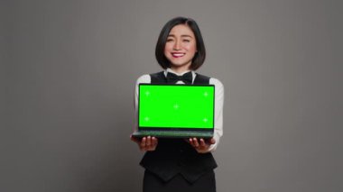 Kişisel dizüstü bilgisayarda yeşil ekran görüntüsü gösteren resepsiyonist, ekranda izole edilmiş bir telif alanı modeli sunuyor. Asyalı otel çalışanı elinde kromakey model şablonuyla bilgisayar tutuyor. Kamera A.