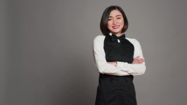 Restoran hostesi. Stüdyoya güvenerek poz veriyor. Gri arka planda kollarını kavuşturmuş duruyor. Kameraya gülümseyen bir gurme ile Asyalı garson garson. Kamera A.