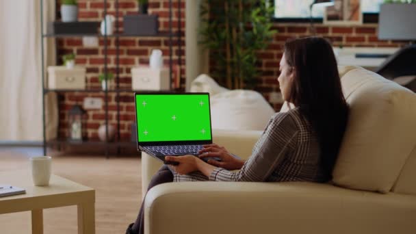 セルフは ソファーからさまざまな仕事をするために 緑色のスクリーンラップトップを使用して自宅にいる女性を雇いました クロマキーノートのキーボードにデータを入力するリモートワーキングインド人 — ストック動画