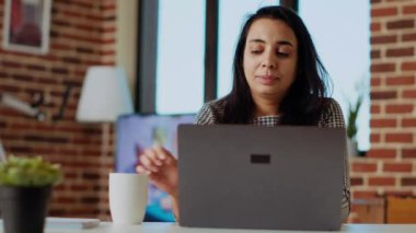 Teleworker dizüstü bilgisayarından e-postalarını kontrol ediyor ve kahvenin tadını çıkarıyor. Uzaktan kumandalı çalışan şık, rahat bir dairede çalışıyor. Özel ofis, sıcak içecek, kamera B.