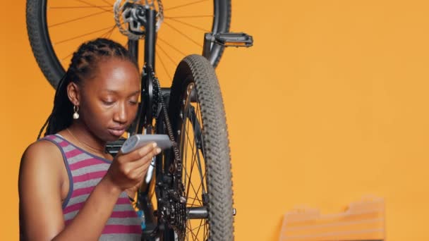 壊れた自転車チェーン スタジオの背景を修復するために特別な接着剤を使用するアフリカ系アメリカ人女性 メンテナンスプロセス中に自転車部品に接着剤を適用する熟練エンジニア カメラA — ストック動画