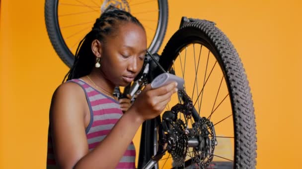 壊れた自転車チェーン スタジオの背景を修復するために特別な接着剤を使用するアフリカ系アメリカ人女性 メンテナンスプロセス中に自転車部品に接着剤を適用する熟練エンジニア カメラB — ストック動画