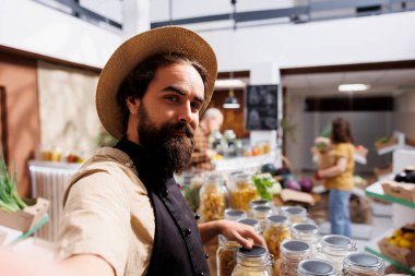 Çevre dostu vegan ürünleri internette tanıtmak için cep telefonunda selfie kamerasıyla gülen sıfır atık dükkânı girişimcisi. Düşük karbonlu ayak izi süpermarket sahibi pazarlama içeriğini filme alıyor