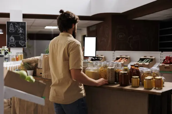 零废品商店的顾客使用模拟平板电脑查找与食物有关的信息 携带隔离屏蔽器的人在当地的杂货店里查阅含有发现的配料的健康食谱 — 图库照片