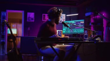 Ses mühendisi elektrikli sentezleyicinin tuşlarına basıyor ve yeni müzik kaydediyor, ses seviyesini ayarlıyor. Sanatçı mikrofonda şarkı söylüyor. Ev stüdyosunda miksaj masasında çalışıyor. Kamera B.