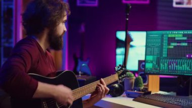 Ev stüdyosunda yeni bir parça için gitar sesi kaydeden bir müzisyen, ses paneli kontrolleri ve bilgisayardaki daw yazılımı. Genç müzisyen akustik enstrüman çalıyor, müzik endüstrisi. Kamera A.