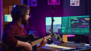 Ev stüdyosunun elektronik düzeneği ile çalışan müzik yapımcısı akustik gitar sesleri kaydediyor. Sanatçı sinyal işleme etkinliğini yönetir, masadaki dijital ses çalışma istasyonunu kullanır. Kamera A.