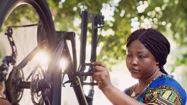 Siyahi kadın, yaz bisikleti için tekerlek ve pedalları test ediyor. Afrika kökenli Amerikalı kadın bisikletçi beyaz bir adamla bisiklet parçalarını tamir etmek için iş aletleri kullanıyor..