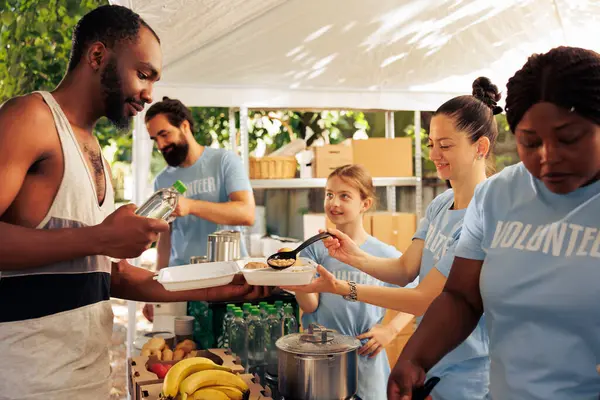 stock image Young african american and caucasian volunteers donate free food and essential items to the less fortunate. Friendly voluntary people provide hunger relief and humanitarian aid at homeless shelter.