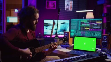Laptop, akustik gitar çalmayı öğrenmek için eğitim programları ve çevrimiçi dersler izlemeyi öğrenen müzisyenlerin yeşil ekran kromatonlarını gösteriyor. Ev stüdyosunda gitar eğitimi alan bir sanatçı. Kamera B.