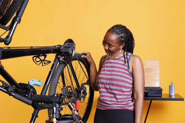 专门的黑人妇女检查自行车轮胎损坏情况 以便用专业的工作工具进行修理 用专用设备在破碎的自行车胶轮上工作的活跃的非洲裔美国女性 — 图库照片