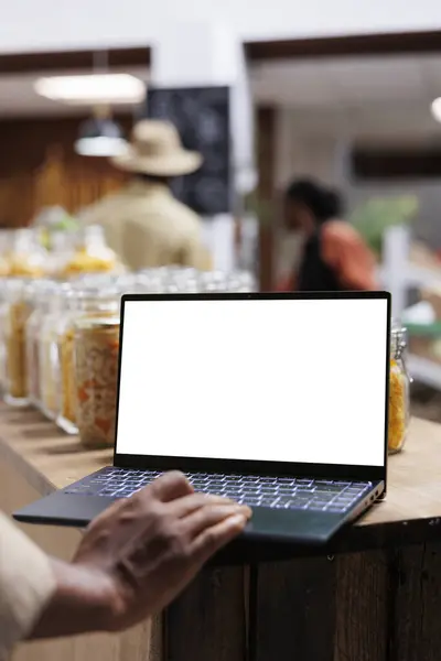 エコフレンドリーなスーパーマーケットで孤立したコピースペースのモックアップテンプレートを示すデジタルラップトップの詳細なビュー 空白の白いスクリーンの表示が付いているミニコンピューターを使用するアフリカ系アメリカ人のクローズアップ — ストック写真