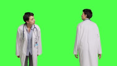 Kontrol muayenesine gelecek hastaları arayan bir kadın doktor, yeşil perdeye karşı duran birini bekliyor. Beyaz önlüklü pratisyen hekim sabırsızlanıyor. Kamera B.