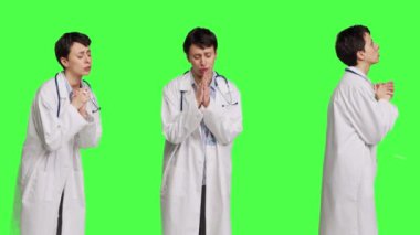 Umut dolu doktor yeşil perde arkaplanına karşı dua işareti yaparak stüdyoda barış ve af diliyor. Beyaz önlüklü kadın doktor meditasyon yapıyor. Kamera B.