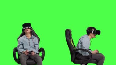 Kadın kumanda ve vr kulaklıkla konsolda video oyunları oynuyor, yeşil ekran arka planına karşı oturuyor. Oyuncu çevrimiçi turnuva, sanal gerçeklik etkileşimli siber uzay ile eğleniyor. Kamera B.