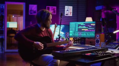 Erkek söz yazarının portresi akustik gitar çalıyor ve ev stüdyosunda müzik sesi kaydediyor. Dijital sesli çalışma istasyonu yazılımı ile melodiler bestelemek. Kamera B.