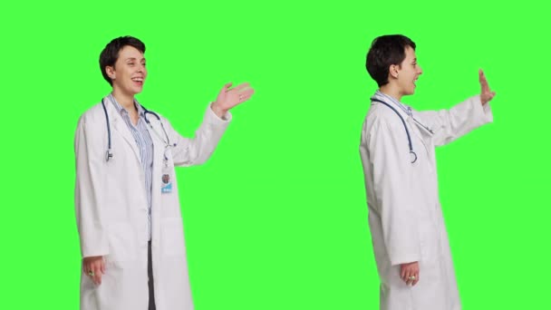 友好的医生在绿屏的背景下挥手致意和问候病人 在她的考试预约前微笑 穿着白衣的女医生欢迎人们 并感到快乐 摄像头B — 图库视频影像