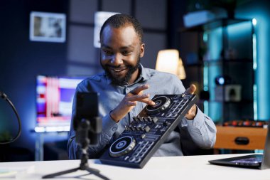 Gülümseyen BIPOC sanatçısı DJ 'i kayıt stüdyosunda karıştırıyor, pikaplarla, örneklerle ve ses efektleriyle oynuyor. Müzik prodüksiyon içeriği yaratıcısı izleyicilere ses donanımı gösteriyor