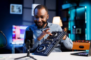 Smiling BIPOC artist filming DJ mixing tutorial in recording studio, playing with turntables, samples and sound effects. Music production content creator showcasing audio equipment to audience clipart