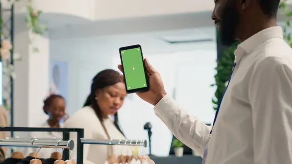 アフリカ系アメリカ人男性は スタイリッシュなフォーマルウェアの服を着たプレミアム衣料品店で携帯電話をモックアップしています デザイナーのショールームの緑のスクリーン携帯電話が付いているBipocの顧客 — ストック写真