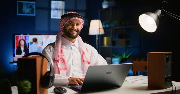 ハッピーアラビアのテレワーカーはスタイリッシュなアパートで求人メールに答えます 穏やかなイスラム教徒の従業員はリモートで働き バックグラウンドノイズ ハンドヘルドカメラのショットとして開かれたテレビとラップトップ上のデータを入力します — ストック写真